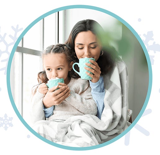 mother and daughter sipping hot chocolate in front of a window while wrapped in a blanket