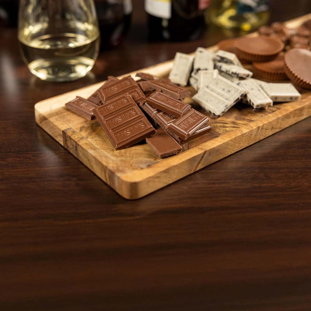 board topped with an assortment of unwrapped hersheys candies beside glasses of wine